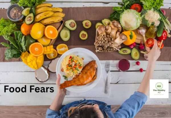 Top-down view of a colorful fruit and veggie spread with a plate of roasted fish; a person reaches for food, text reads 'Food Fears' on the image.